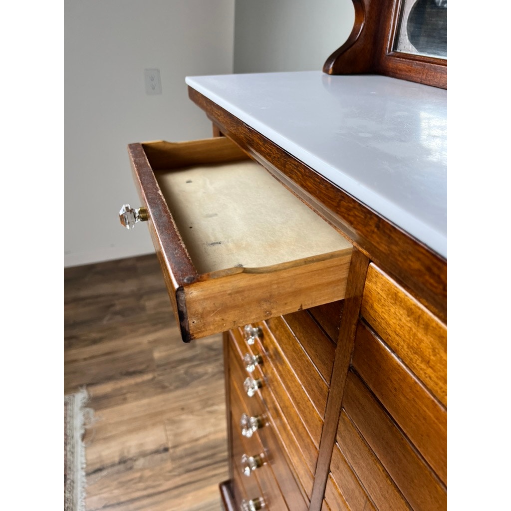 A close-up of an open drawer in an Antique Mahogany Multi-drawer Dental Cabinet by The American Cabinet Co. (early 20th c.), with a glossy white top, glass knobs, attached mirror, and light interior.