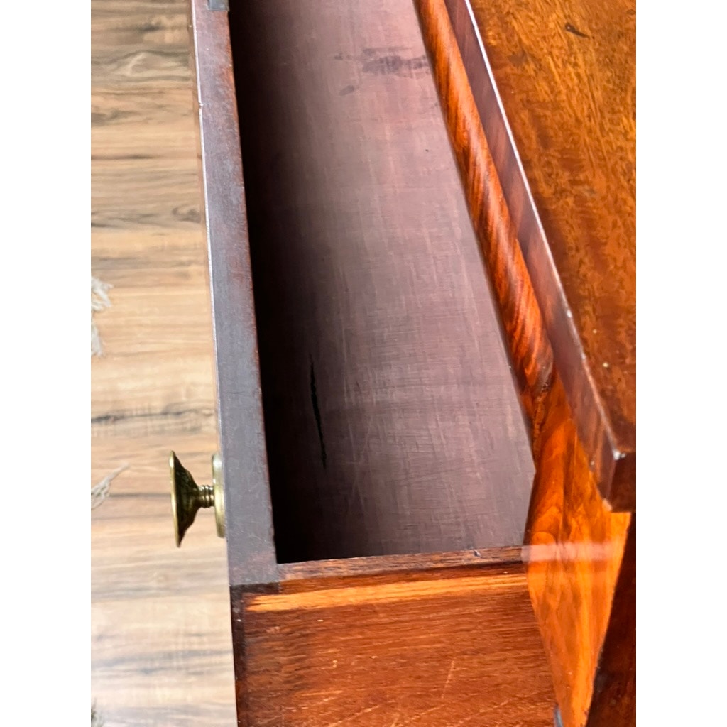 An open drawer with a brass knob reveals its empty interior in the Antique American Empire Albany Four Drawer Chest c. 1840. The polished wood surface and medium-toned, grainy floor complete the classic look. Brand: None/Unknown.
