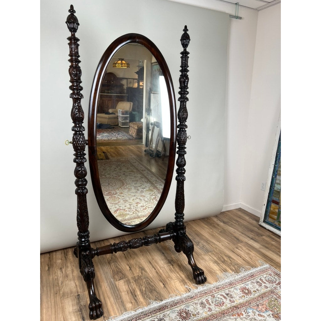The Impressive Antique American Empire Acanthus and Barbola Rose Carved Cheval Mirror c. 1840 with dark wood, claw feet, and ornate carvings stands on a hardwood floor beside a patterned rug and white wall in a well-lit room.