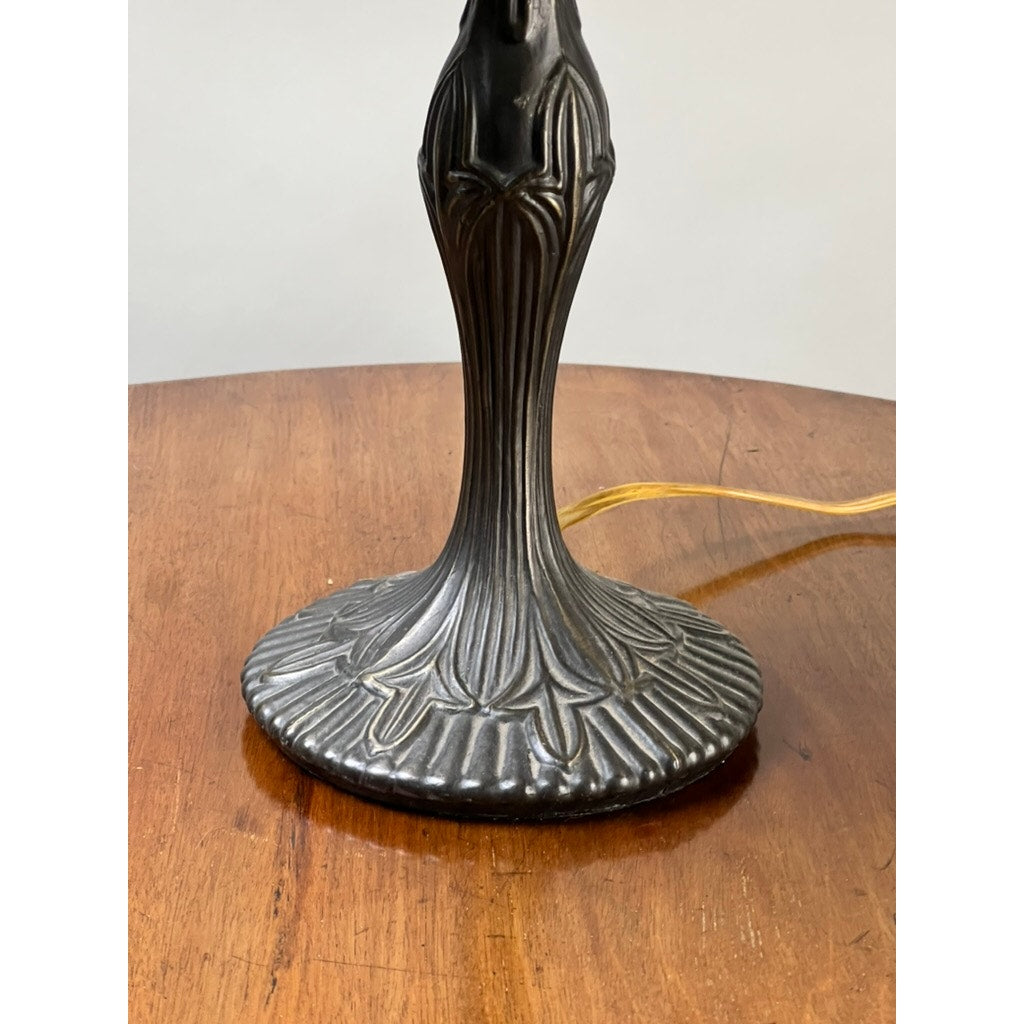 A close-up of the ornate base from a Vintage Tiffany Style Floral Stained Glass Table Lamp, featuring a dark metallic, textured design on a wooden table with a yellow power cord extending from the base. Brand is unknown.