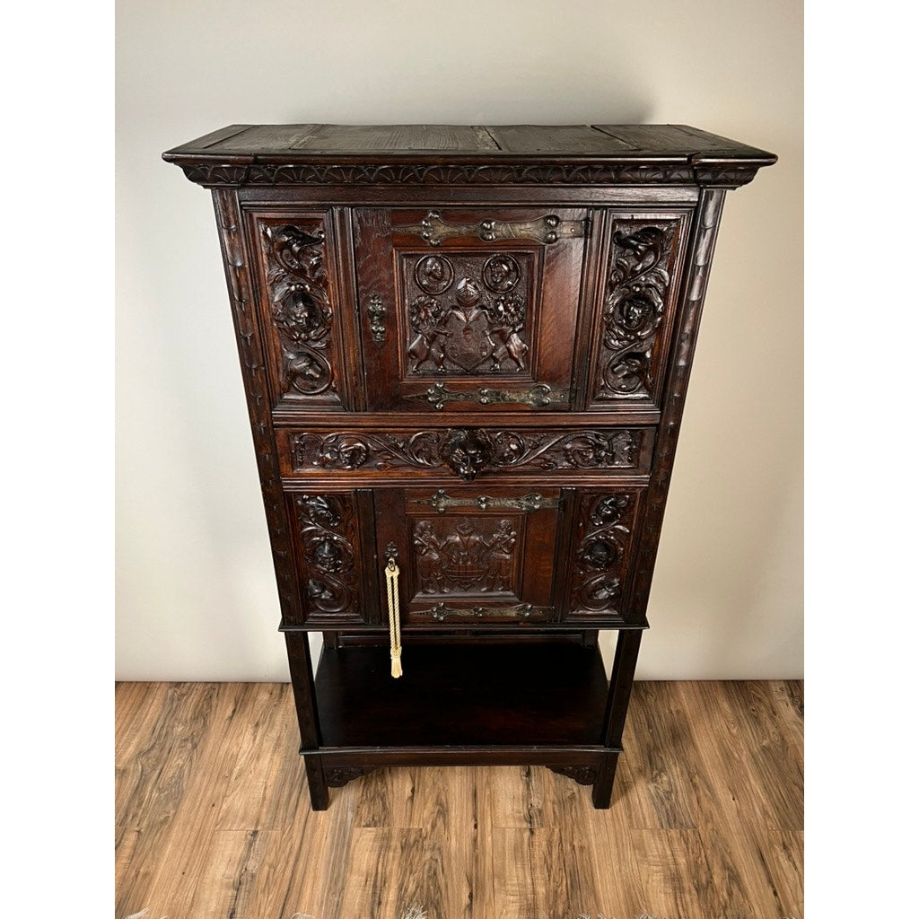 An Antique 19th-Century French Breton-Style Carved Oak Cabinet featuring deeply carved knights stands on a wooden floor against a plain, light-colored wall, highlighting the timeless elegance of antique craftsmanship.