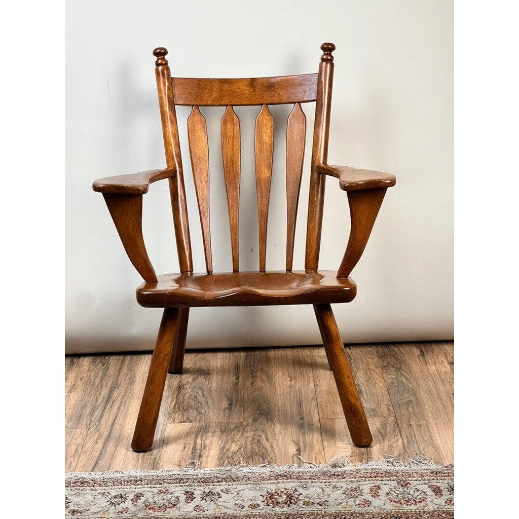The Vintage Herman DeVries for Cushman No. 5-82 Rock Maple Easy Chair by Cushman features a curved seat, vertical slats, wide armrests, and angled legs, shown on a wood floor beside a patterned rug and light-colored wall.