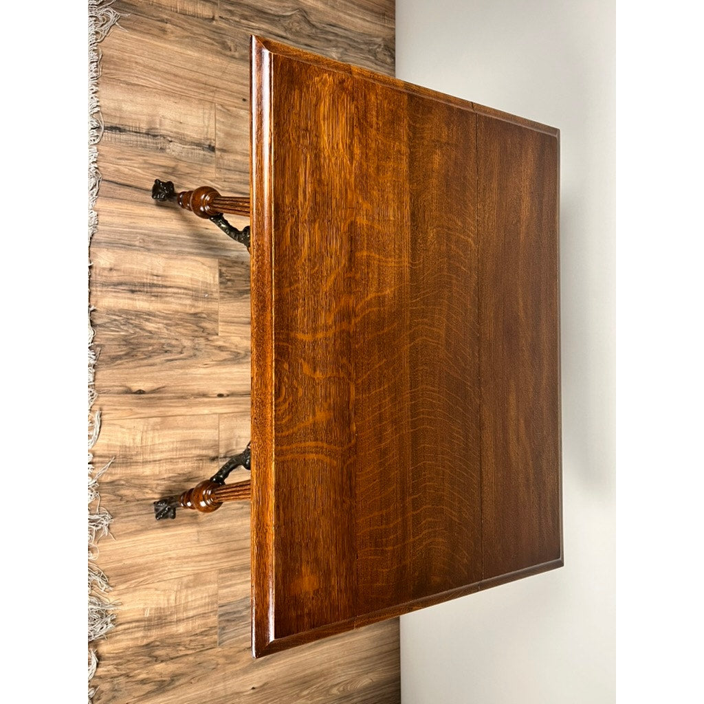 A polished wooden table with ornate carved legs stands on a wooden floor, next to an Antique Victorian Oak Lamp Stand with Bronze Lions Head Mountings (late 19th century) and a fringed rug visible at the image’s left edge.