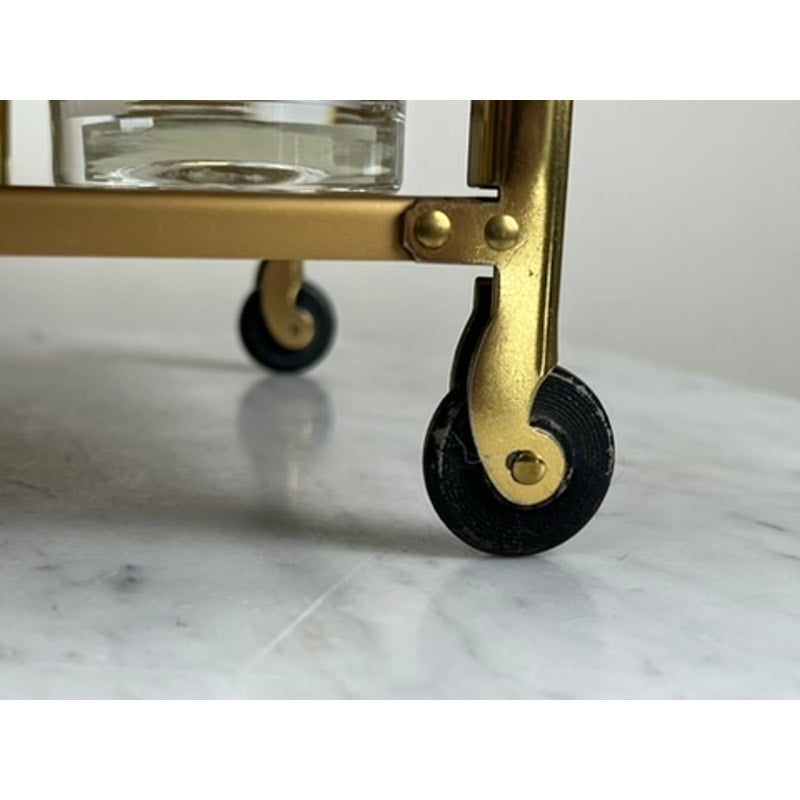 Close-up of a small black wheel on a Vintage Mid Century Modern Bar Caddy (c. 1960s) supporting a glass container, all resting on a white marble surface; brand unknown.