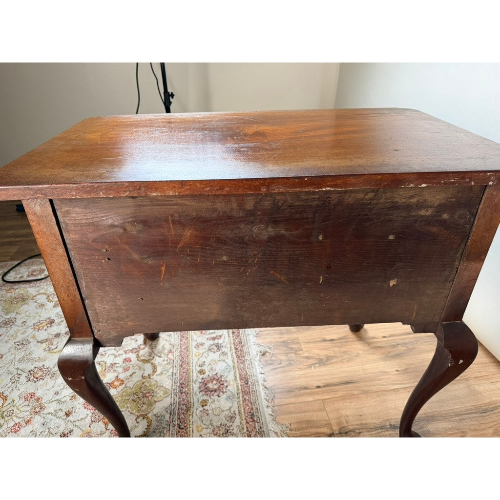 An 18th Century American Queen Anne Walnut Shell-Carved Lowboy (c. 1740–1770), featuring curved legs and a worn finish with visible scratches on the front, stands on a patterned rug and wood floor near a white wall.