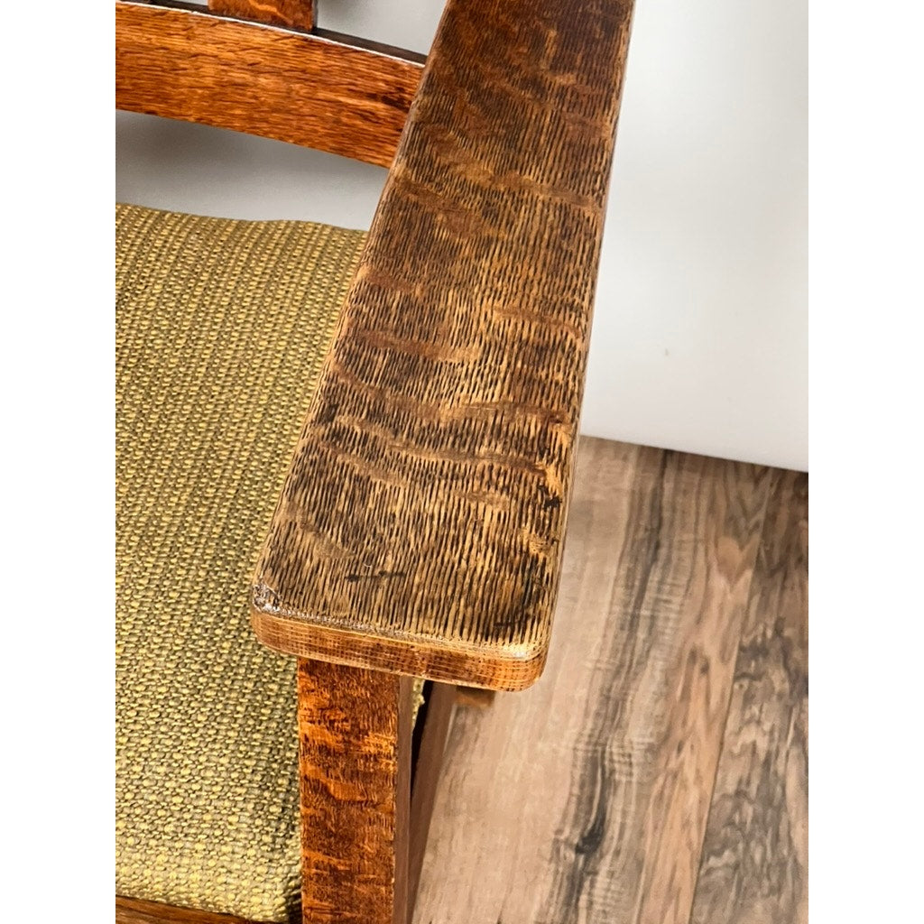 Close-up of an Antique Quarter Sawn Mission Oak Arm Chair by Quaint Furniture c. 1920, highlighting its wooden armrest and textured mustard-yellow cushion on a grain-patterned wooden floor.