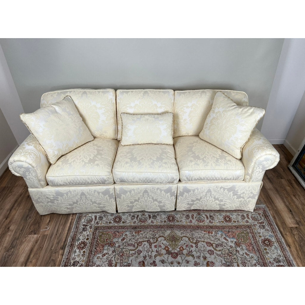 A Vintage Custom Ivory Upholstered Sofa by Stickley sits against a pale wall on a wooden floor, with an ornate rug in front. The ivory sofa features three seat cushions and matching pillows, showcasing timeless Stickley craftsmanship.