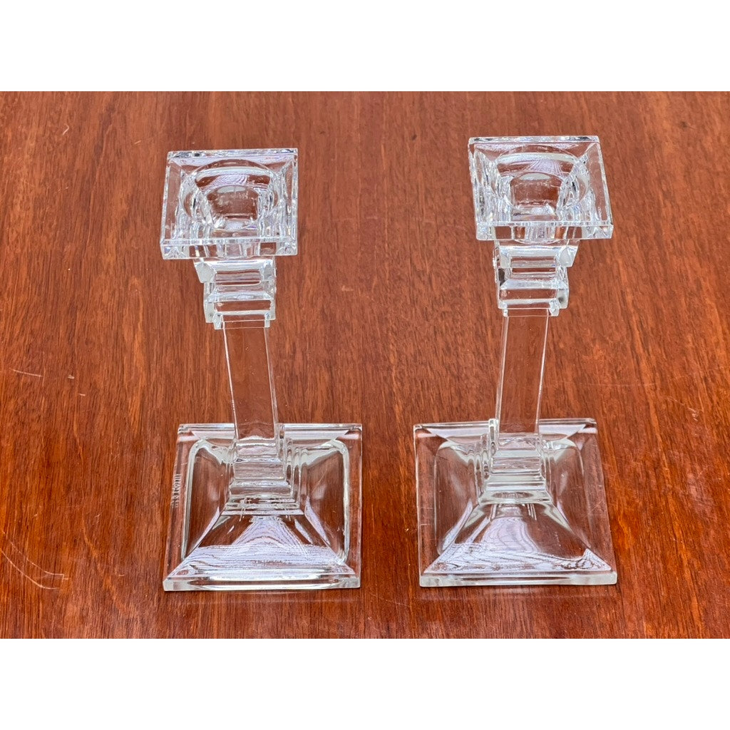 A Vintage Pair Tiffany & Co. Clear Crystal Candlesticks, featuring square bases and tops, are displayed side by side on a wooden surface, showcasing classic elegance from the renowned brand Tiffany & Co.