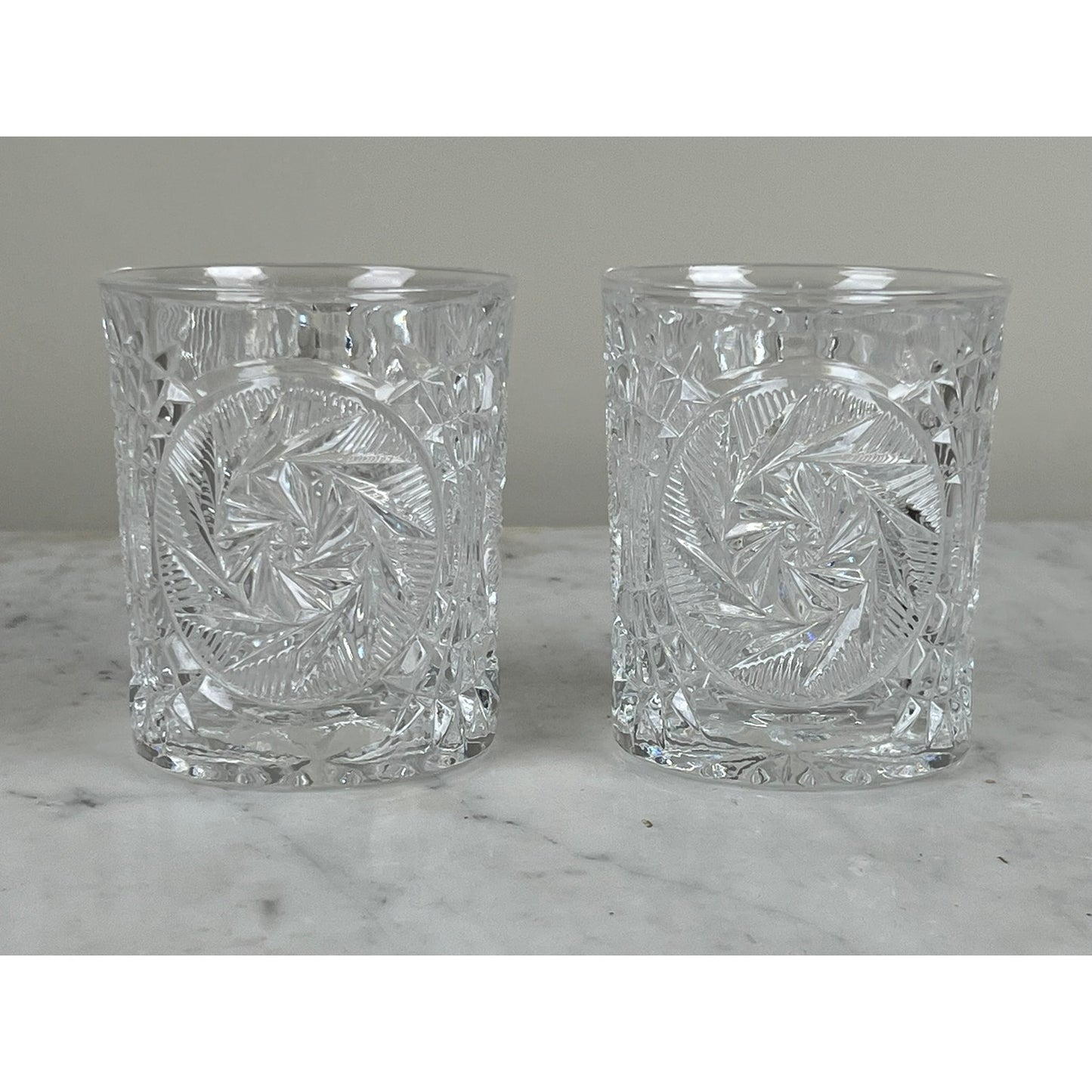 A pair of Fostoria Stowe Double Old Fashioned Tumbler Glasses, featuring intricate geometric swirl patterns, are displayed side by side on marble—classic vintage American glassware from the Fostoria Stowe brand.