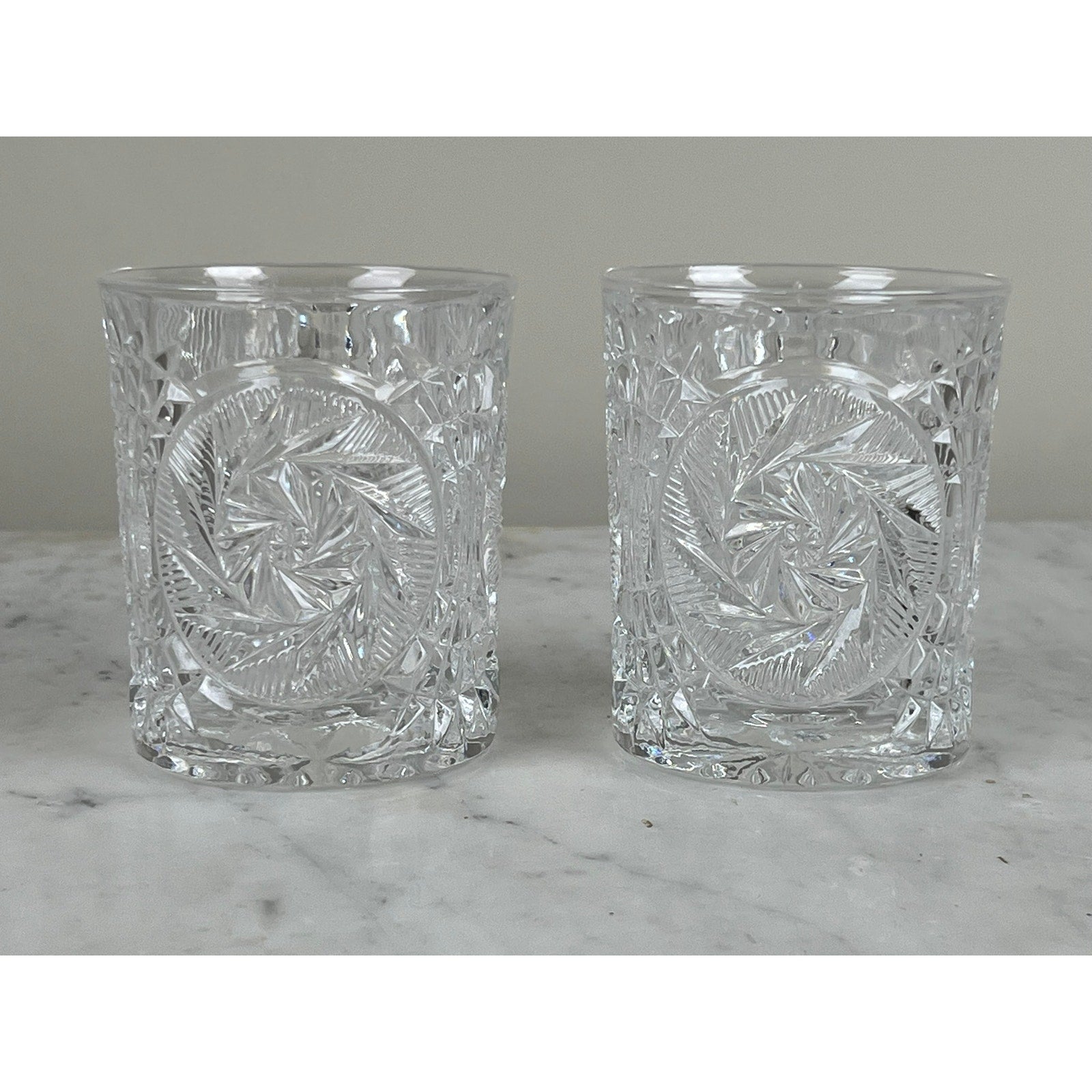 A pair of Fostoria Stowe Double Old Fashioned Tumbler Glasses, featuring intricate geometric swirl patterns, are displayed side by side on marble—classic vintage American glassware from the Fostoria Stowe brand.