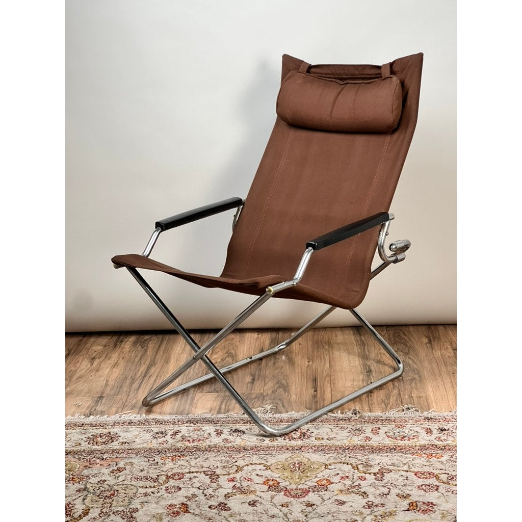 A Vintage Uchida Z Chair Japanese Modern Chrome Sling Lounge Chair with Headrest by Uchida rests on a wooden floor next to a patterned rug, set against a plain light background, showcasing iconic Japanese modern design.