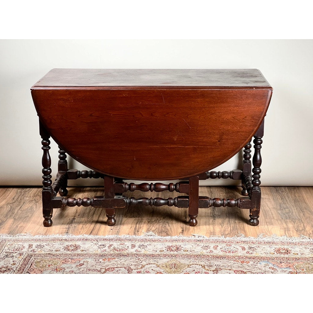 An Antique English William & Mary Walnut One Drawer Gateleg Dining Table (early 18th century), shown with both leaves down, stands on a wood floor next to a patterned rug—a classic example of early English craftsmanship.