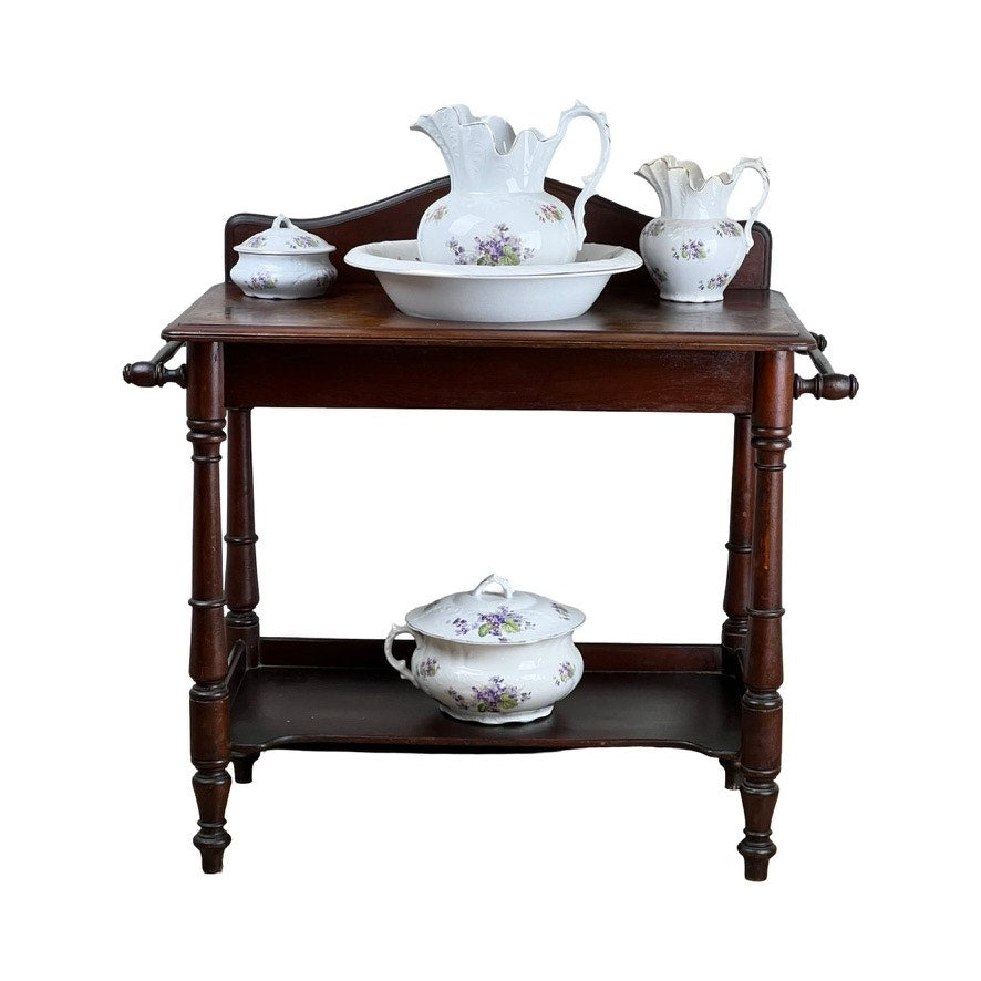 The Antique Victorian Porcelain Wash Stand Set with Stand by Leland, c. late 19th century, features signed white floral washbasins, pitchers, and a covered dish—classic bathroom accessories on a vintage stand.