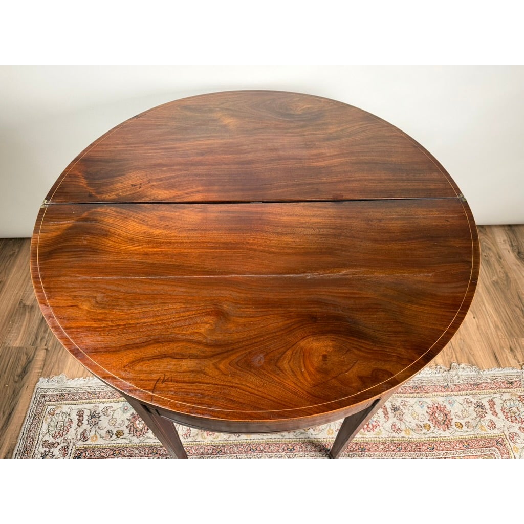 An English George III Mahogany and Satinwood-Inlaid Demilune Games Table in dark mahogany, viewed from above, featuring a rich wood grain with thin light-colored inlay around the rounded edge.
