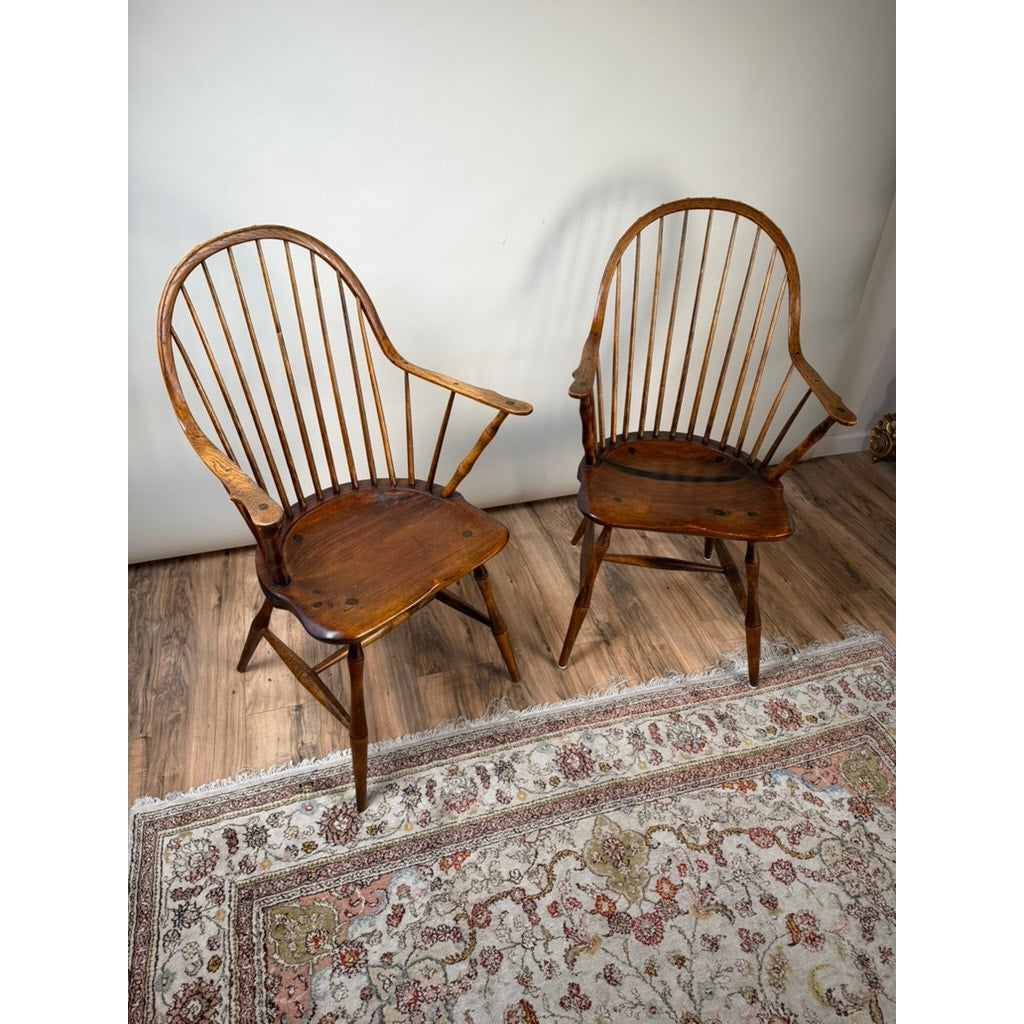 A pair of signed L.E. Partridge Connecticut bench-made continuous-arm Windsor chairs from the 1960s sit side by side on a patterned rug over a wooden floor, set against a plain light-colored wall.