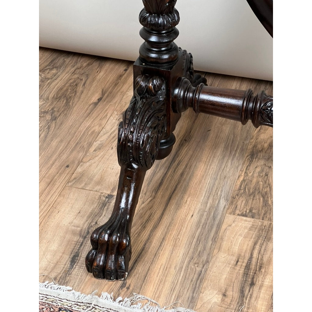 An antique American Empire acanthus and Barbola rose carved cheval mirror c. 1840 features a dark wooden leg shaped like an animal paw with ornate detailing, standing on a wood-patterned floor beside a patterned rug. Brand: Unknown.