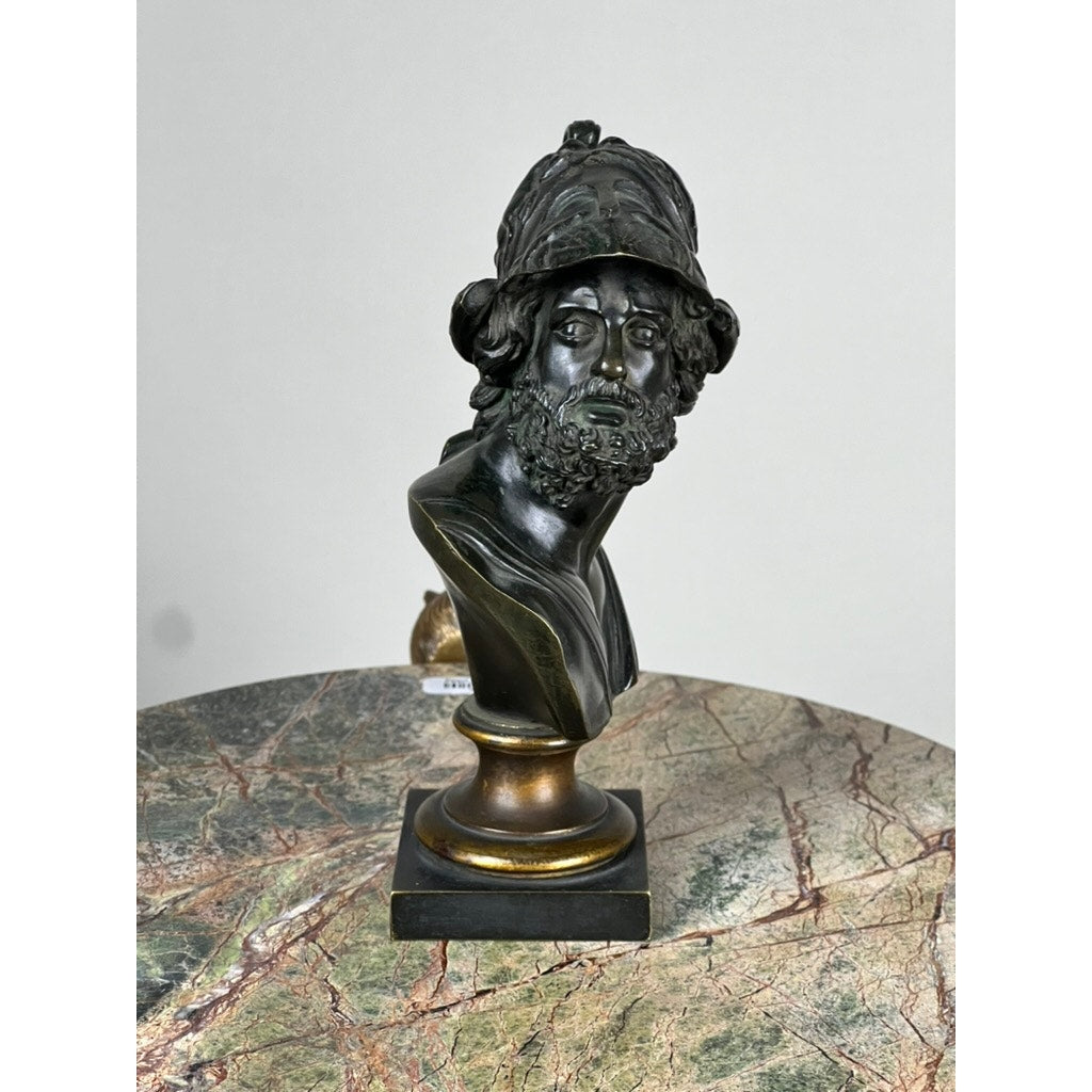 An Antique Small Bronze Bust of King Menelaus, c. Late 19th Century, is displayed on a marble-patterned surface with a plain light gray background. Brand: Unknown.