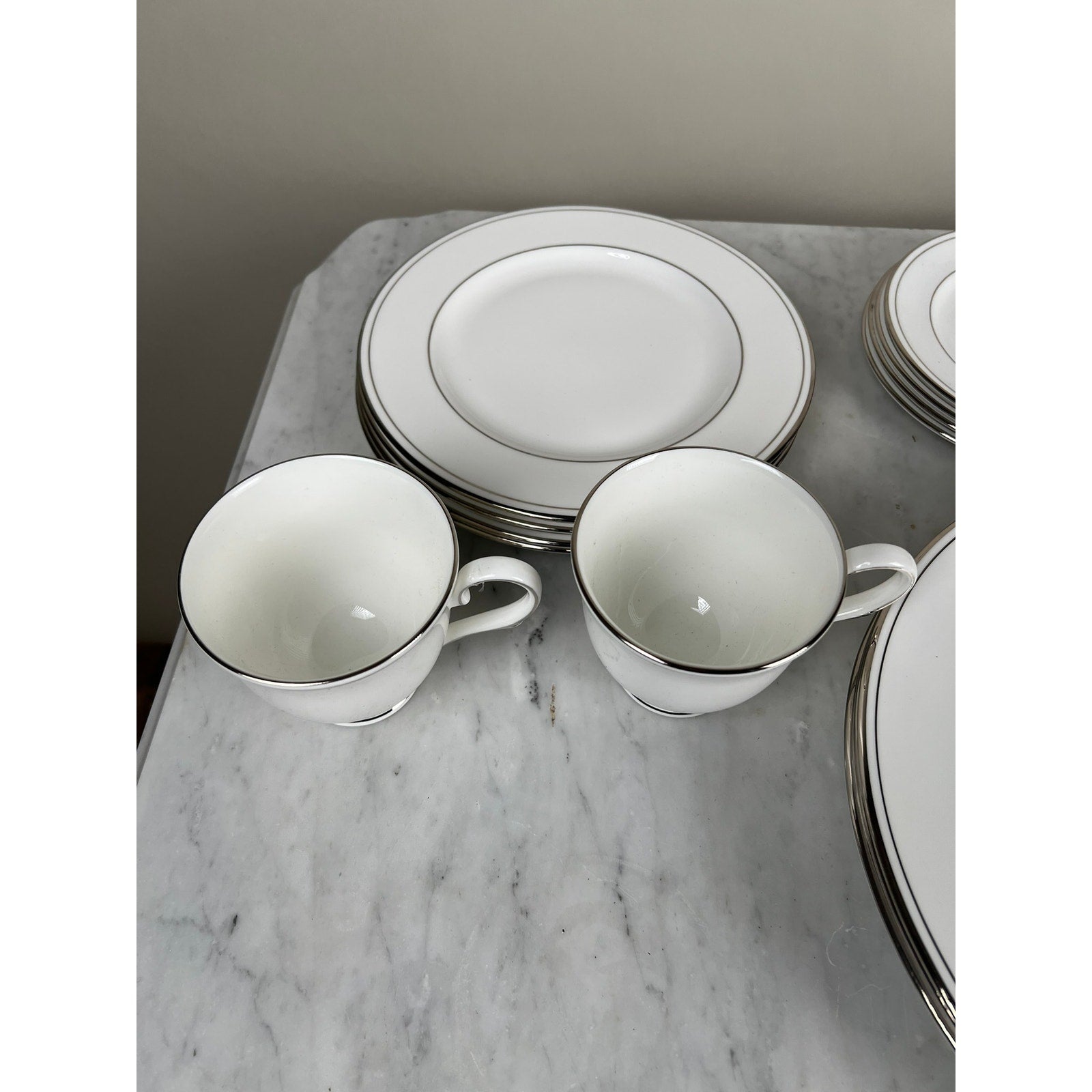 Two white Lenox Federal Platinum Fine English Bone China teacups with platinum rims sit by matching plates on a marble surface. The elegant, vintage Lenox set adds timeless charm to your tableware collection.