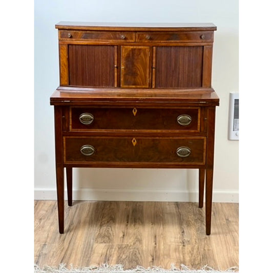 The Antique Federal Mahogany Tambour Secretary c. 1830 features two drawers with brass handles, a hutch with three small cabinet doors, and stands on four tapered legs atop a wooden floor. Brand: Unknown.