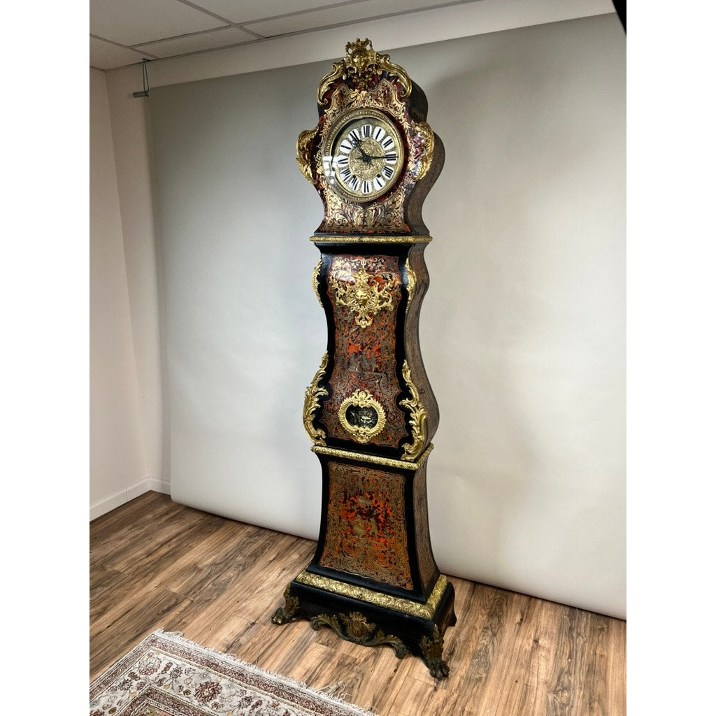 A monumental French Napoleon III Boulle Marquetry floor clock with ormolu mounts, circa 1865–1885, stands on a wooden floor against a plain light-colored wall beside a patterned rug, beautifully showcasing the artistry of 19th-century French decorative design.