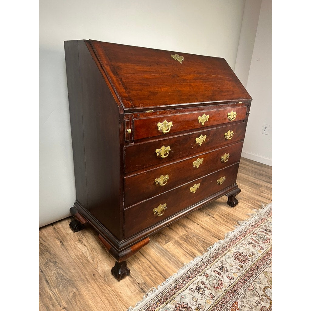 An 18th Century New England Chippendale Cherry Slant Front Desk, circa 1770–1790, crafted from solid cherry with brass handles, three drawers, and decorative claw feet, stands on a wood floor beside a patterned rug—capturing the refined elegance of antique New England design.