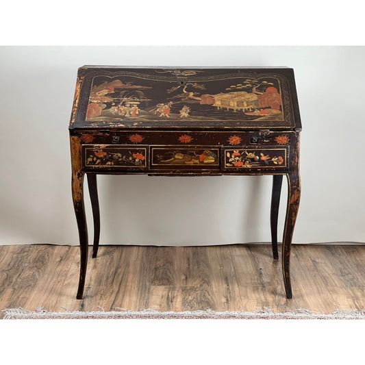 Antique French Louis XV Japanned Fall Front Desk, c. 18th Century by Pearl City Antiques, featuring a black lacquer finish with ornate hand-painted Chinoiserie scenes in the japanned style. The desk is detailed with elegantly curved legs, three small drawers, and a slanted fall front top. Worn areas in the paint reveal the wood underneath, adding to its antique charm.