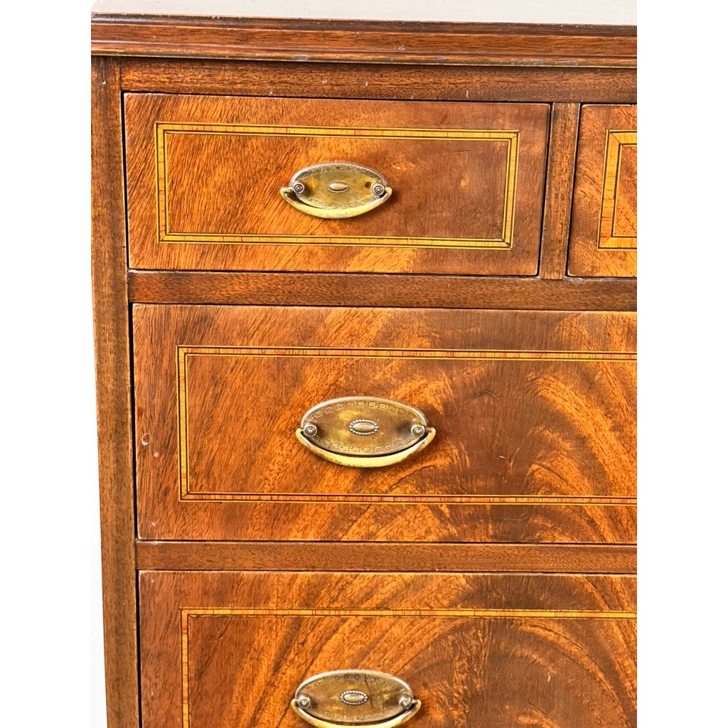 Close-up of the Vintage Dutch Woodcraft Shops Federal Style Flame Mahogany Chest on Stand (c. 1945–1955), showcasing three drawers adorned with brass oval handles and decorative inlaid borders. The striking flame mahogany wood grain and rich finish highlight the fine craftsmanship for which Dutch Woodcraft Shops is renowned.