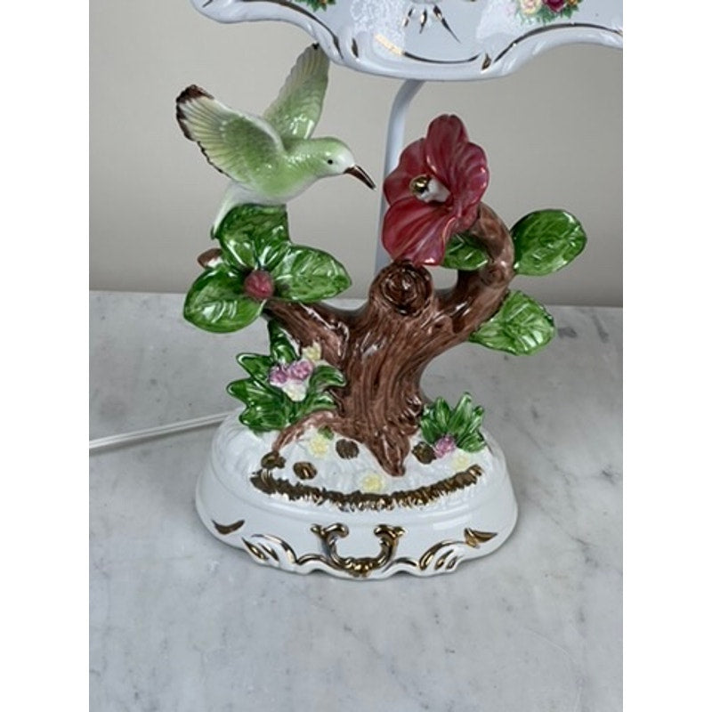 The Vintage Lena Liu Porcelain Hummingbird Accent Lamp features a green hummingbird by a red flower on a branch with green leaves and pink blossoms, all set on a white marble base. Brand: None/Unknown.