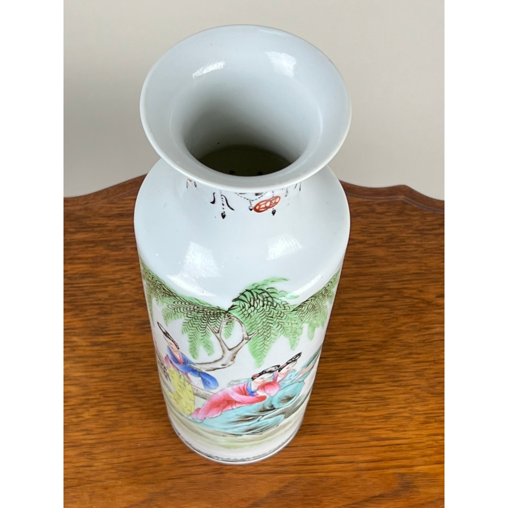 An Antique Qing Dynasty Famille Rose 12” porcelain vase with Qianlong mark, decorated with colorful figures and nature scenes, stands tall with a wide flared rim and white finish on a wooden surface.