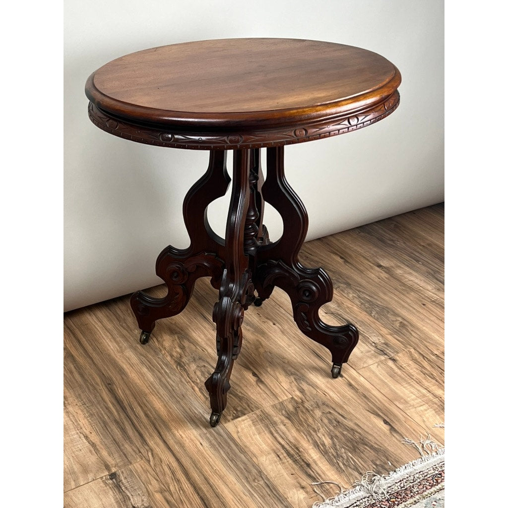 An Antique Victorian Walnut Lamp Stand (late 19th century) with a polished round top and ornate carved legs stands on a wood floor near the edge of a patterned rug. Brand: None/Unknown.