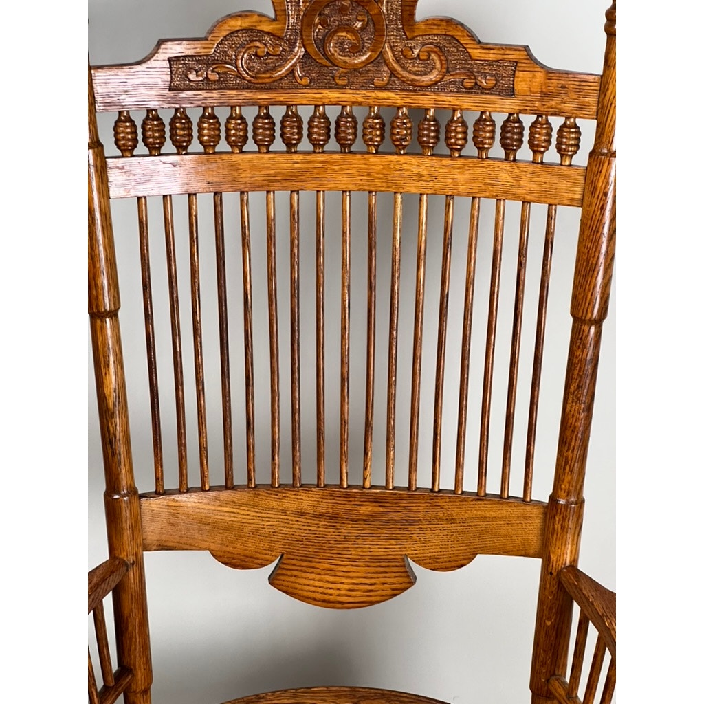 Close-up of the Antique Victorian Oak Platform Rocker c. Late 19th Century shows vertical spindles, ornate carvings, and a glossy finish with decorative scrollwork and turned elements inspired by classic Victorian designs. Brand: Unknown.