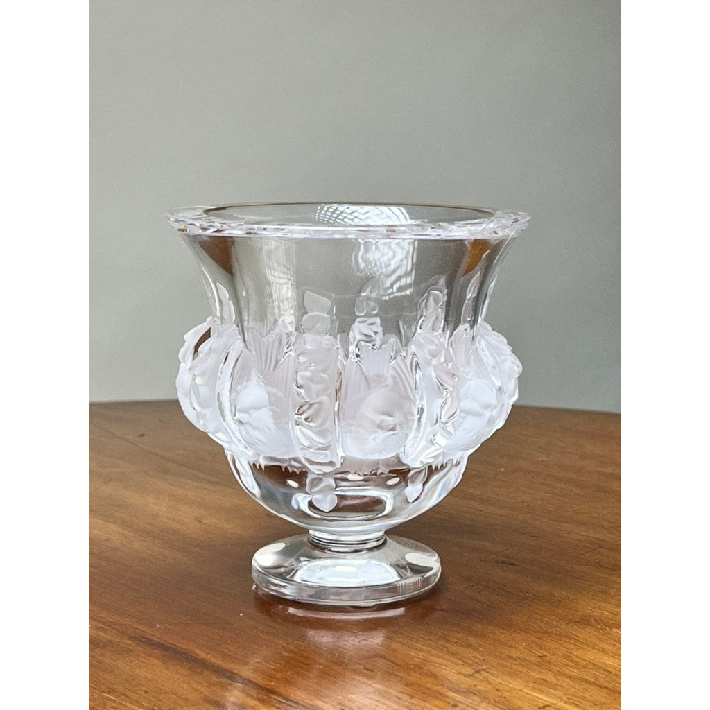 The Vintage Lalique Dampierre Sparrow Footed Vase by Lalique, featuring ornate patterns and a flared rim, sits on a wooden surface against a plain light background, highlighting its classic French crystal design.