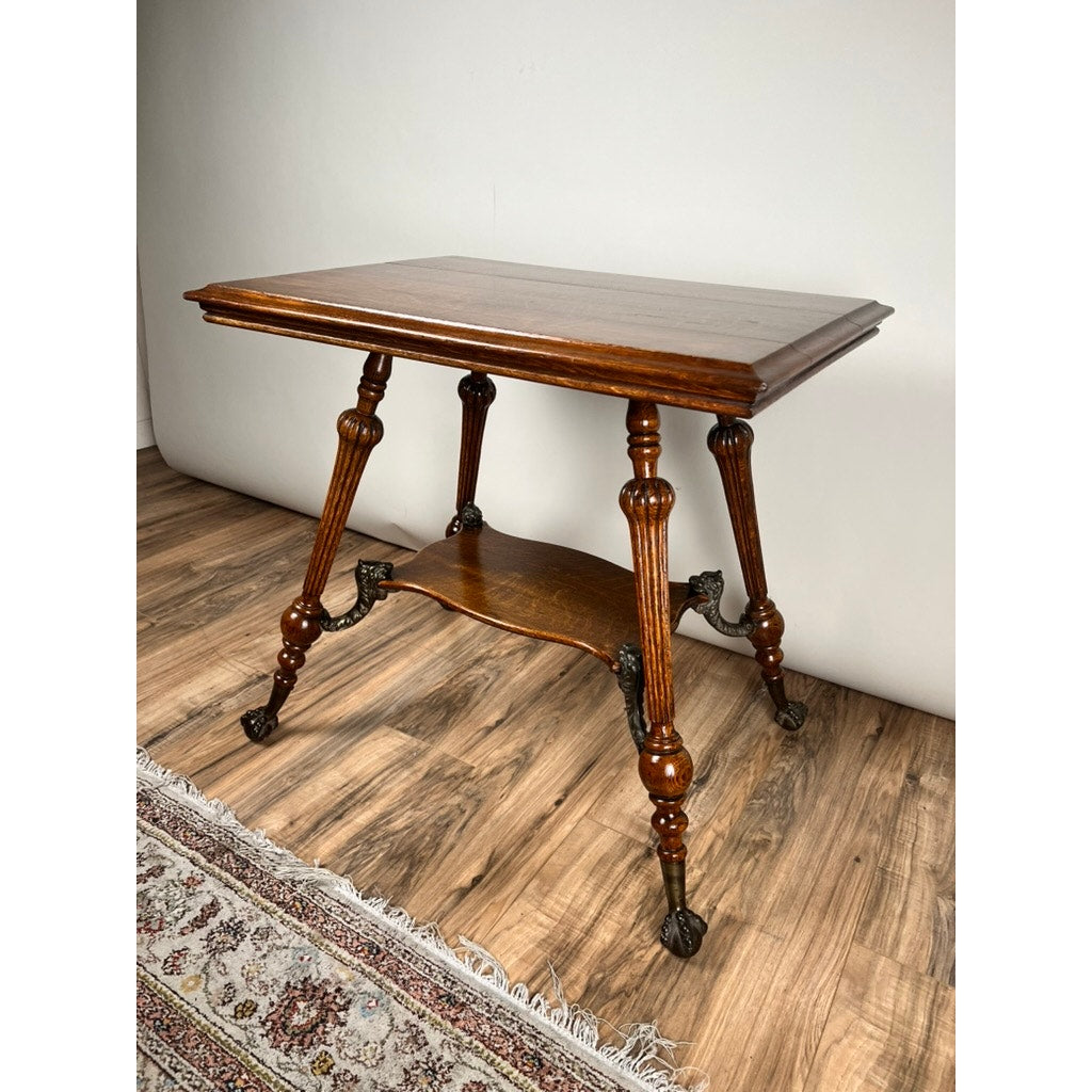An Antique Victorian Oak Lamp Stand with Bronze Lions Head Mountings (late 19th century) sits on a wooden floor beside a fringed patterned rug, against a plain light wall. Brand: None/Unknown.