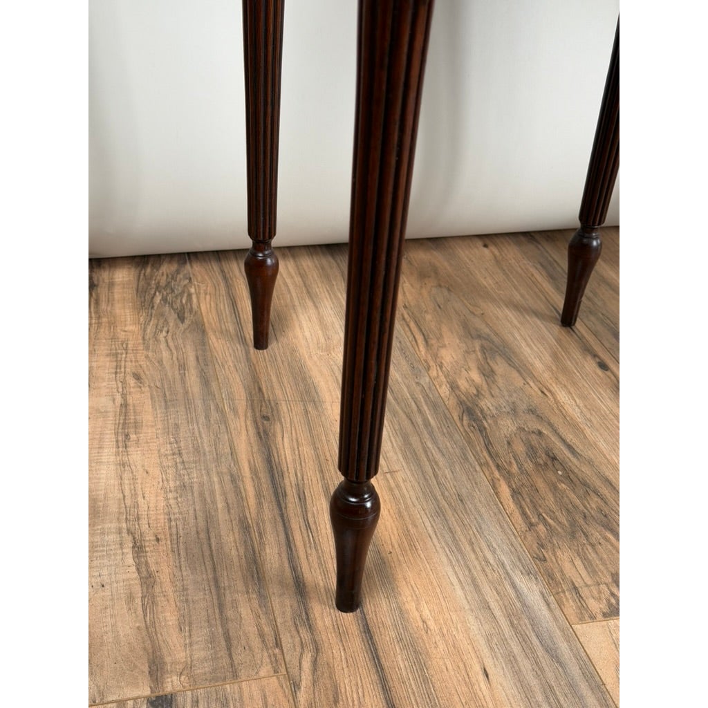 Three dark wood legs from a Pair of American Classical Revival Mahogany Two-Drawer Work Tables, featuring fluted details and tapered feet, standing on a wood floor.