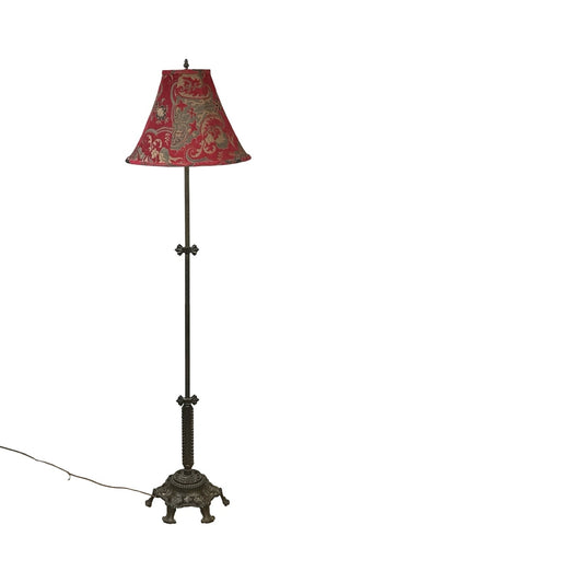 The Rembrandt Antique Art Deco Cast Iron Floor Lamp features an ornate base and red patterned shade, set against a plain white background with its power cord visible.
