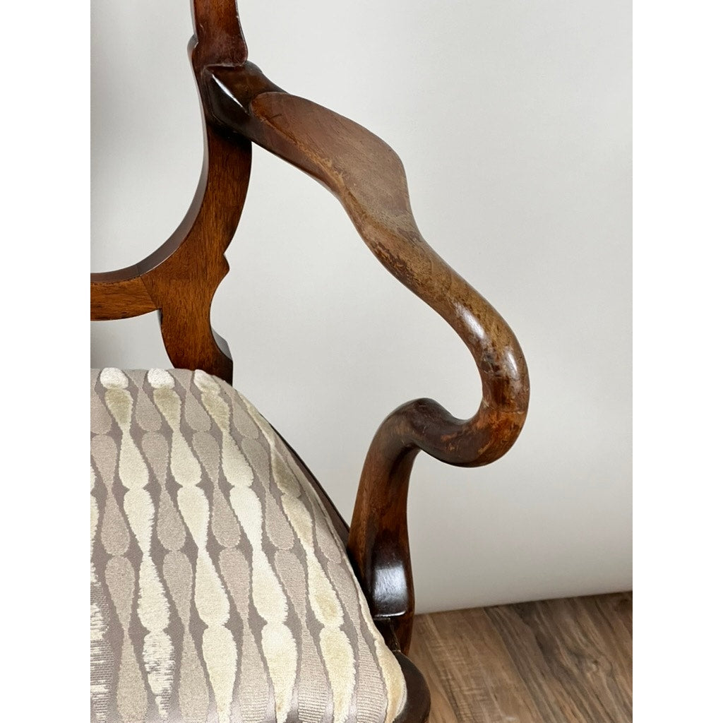 Close-up of an Antique George III Mahogany Open Arm Chair (late 18th century) featuring a curved Chippendale-style wooden armrest and beige oval-patterned upholstery, shown on a wooden floor against a plain light background. Brand unknown.