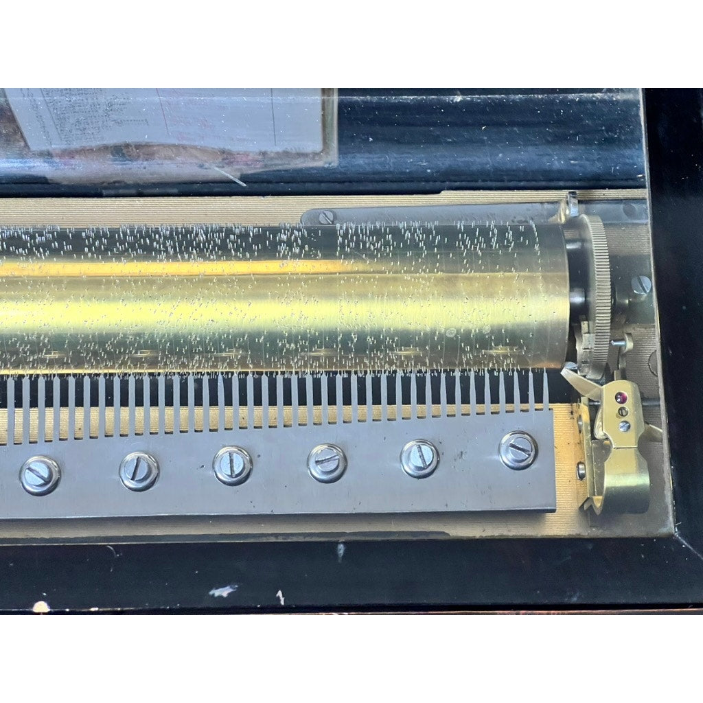 Close-up of an Antique Swiss 12 Tune Music Box from the late 19th century, showing its metal-pinned cylinder and comb under a glass case—an elegant piece with unknown maker.