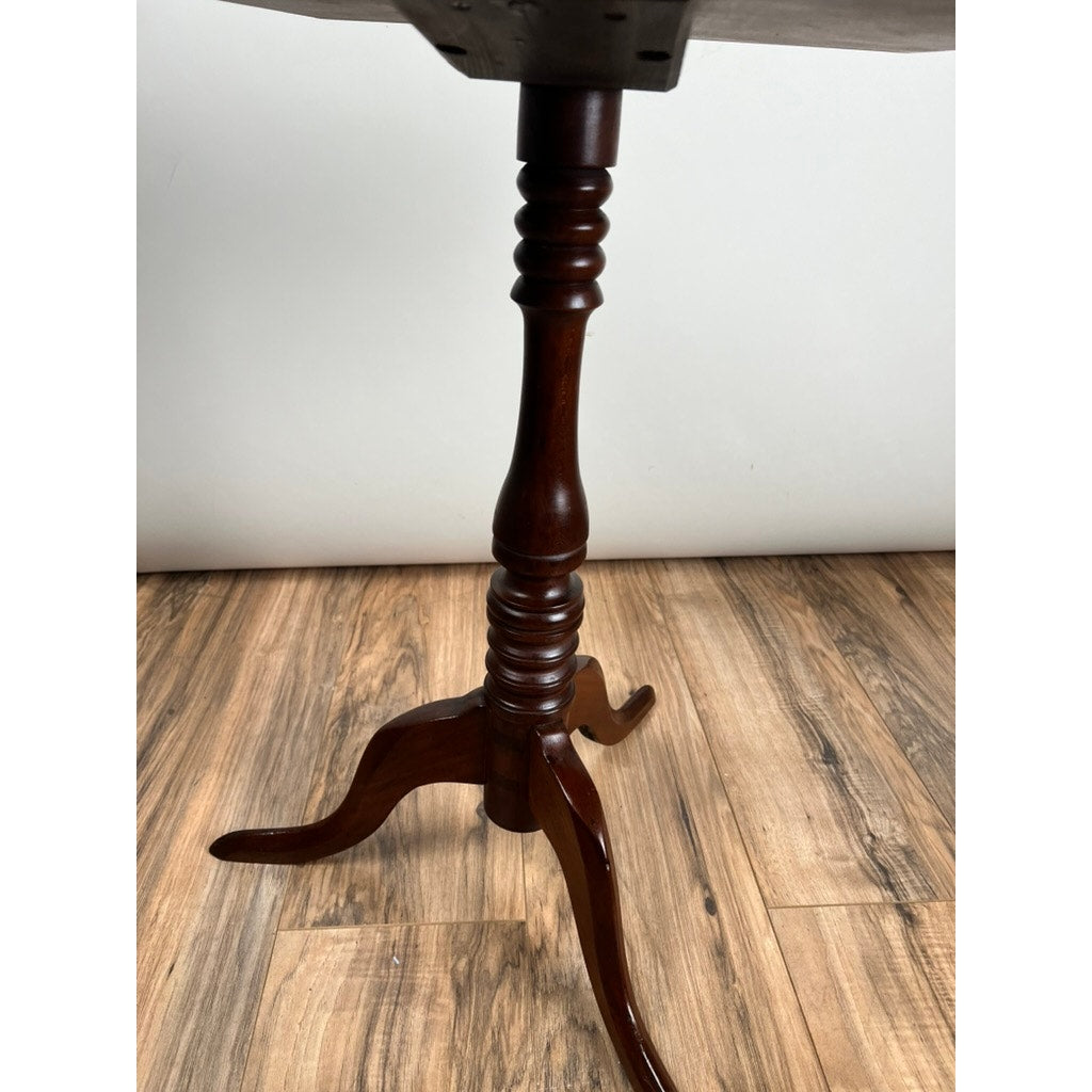 A close-up of the Antique Low Cherry Candle Stand c. Mid 19th Century features its carved pedestal and three curved legs, standing on a wooden floor against a white wall. Brand unknown.