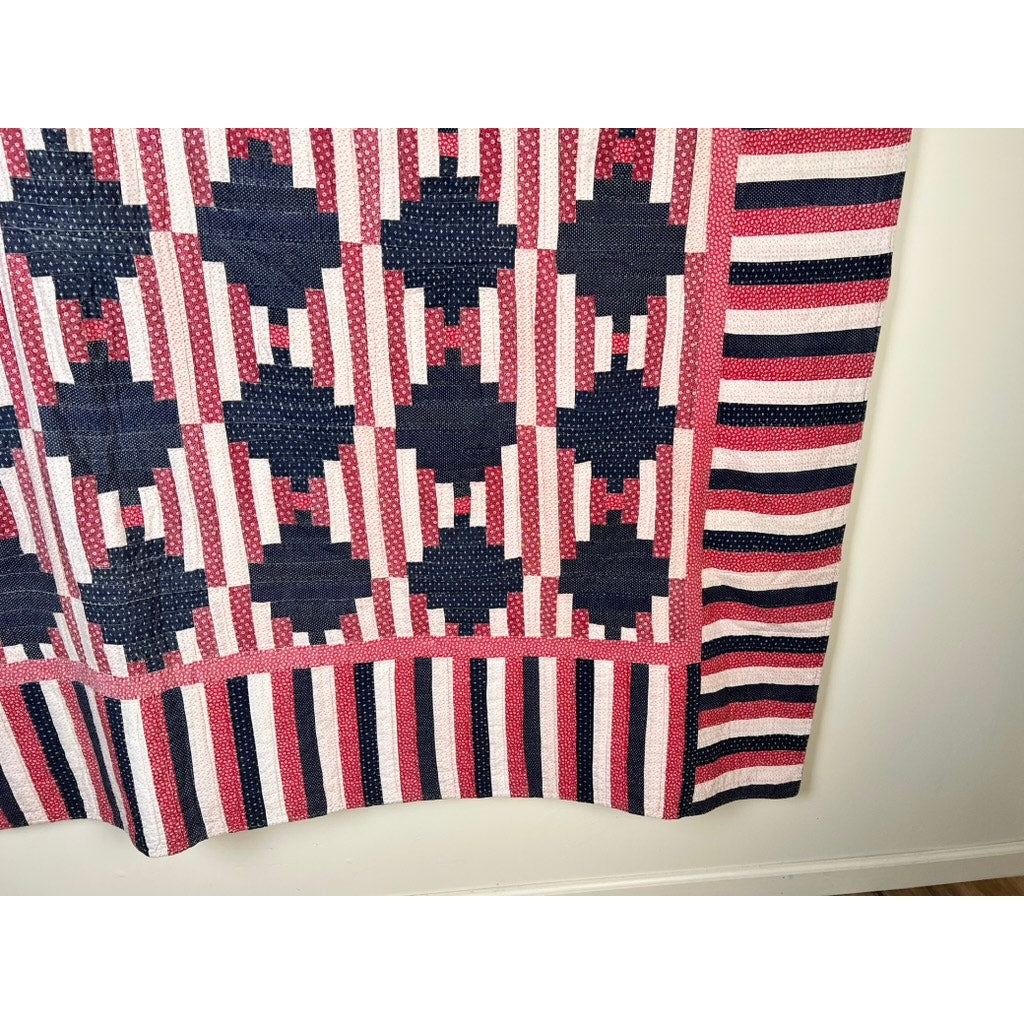 A Matching Pair of Antique American Patriotic Hand Quilted Log Cabin Quilts (early 20th c.) in red, white, and blue hang partially on a wall, with geometric patterns and a striped border on the bottom and right edges.