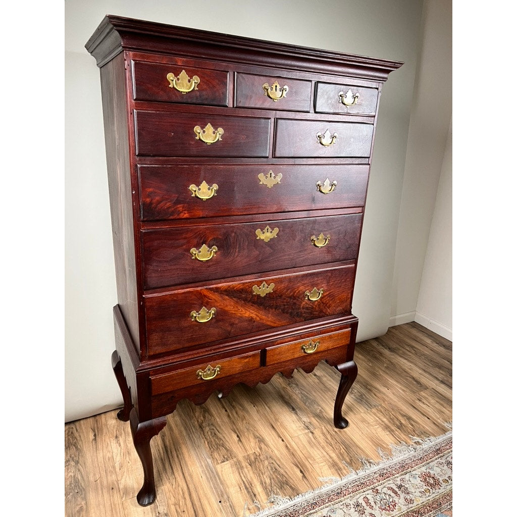 An Antique Queen Anne Walnut Chest on Frame with Drake Feet, probably Irish from the late 18th century, featuring eight drawers and brass handles, stands on curved legs near a beige wall and patterned rug.