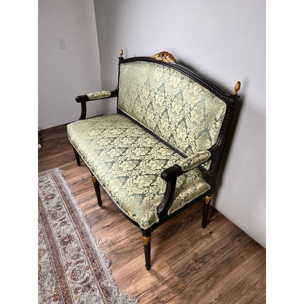 A Vintage Louis XVI Style Settee in green damask upholstery and a dark wood frame sits on a wood floor beside a patterned rug and against a plain white wall. Brand: None and/or Unknown.