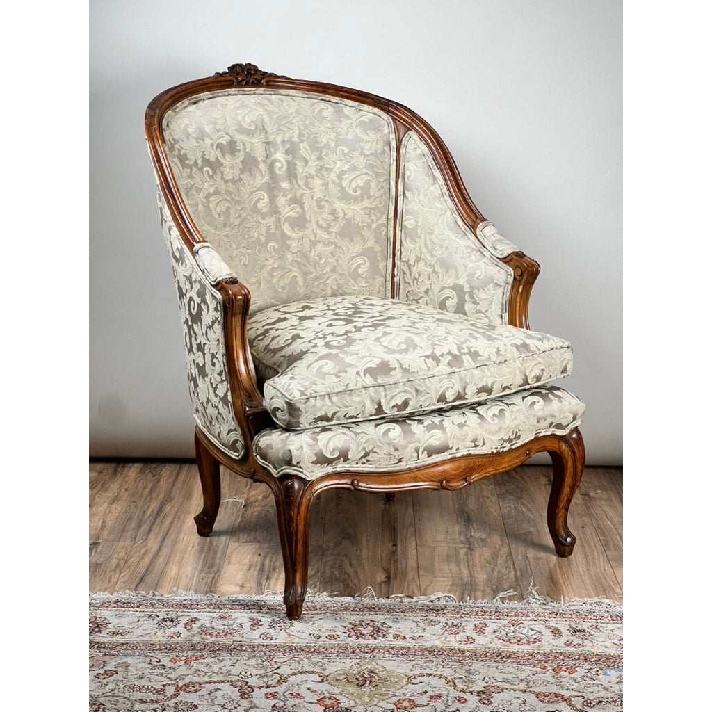 An Antique French Louis XV Rococo Style Bergère Arm Chair in newer damask upholstery (mid 19th century) sits on a wooden floor near a decorative rug. Brand: None or unknown.