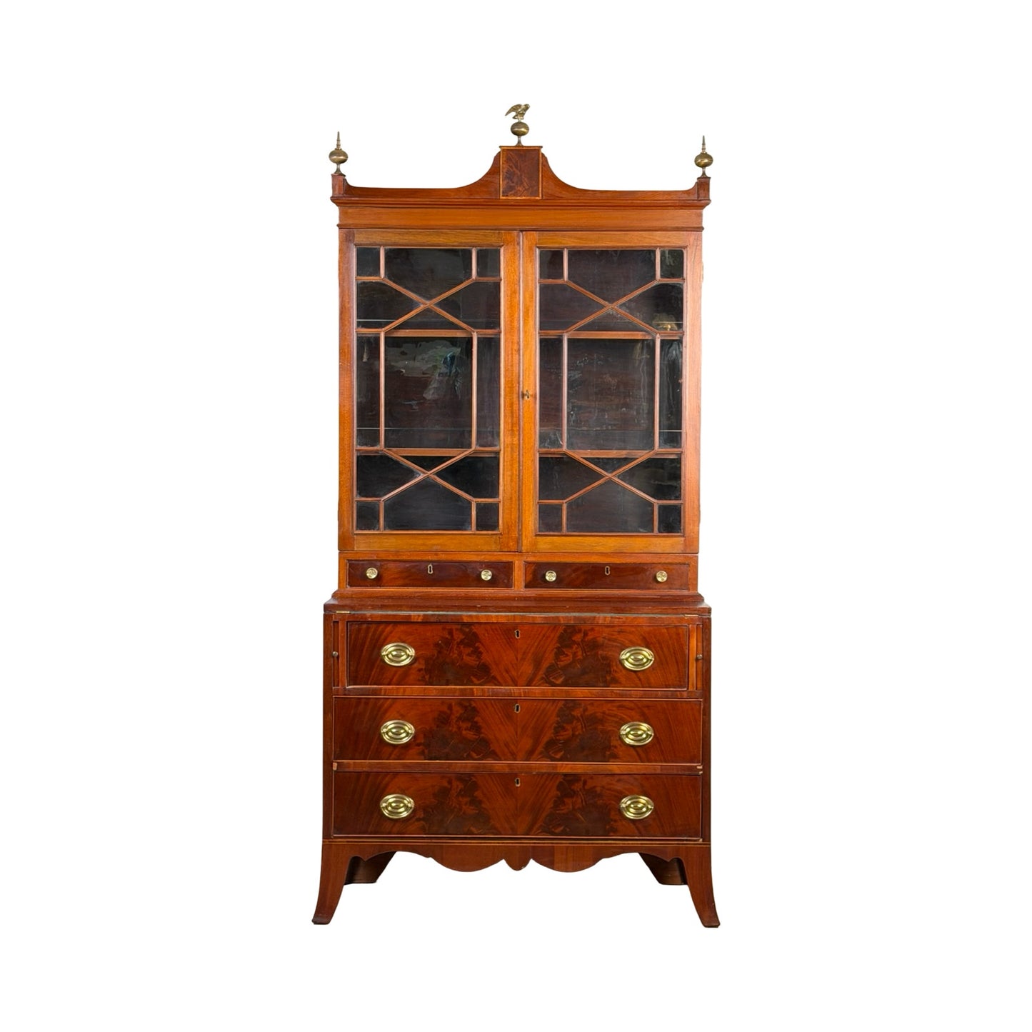 Federal Flame Mahogany Secretary Bookcase with Eagle Finial, c. 1810–1825. This vintage wooden secretary cabinet features glass doors on top with geometric muntins, three spacious drawers below with brass handles, and elegant decorative finials including an eagle finial at the crest. The ornate top and detailed craftsmanship evoke the refined charm of early 19th-century American Federal period furniture. Brand: None/Unknown.