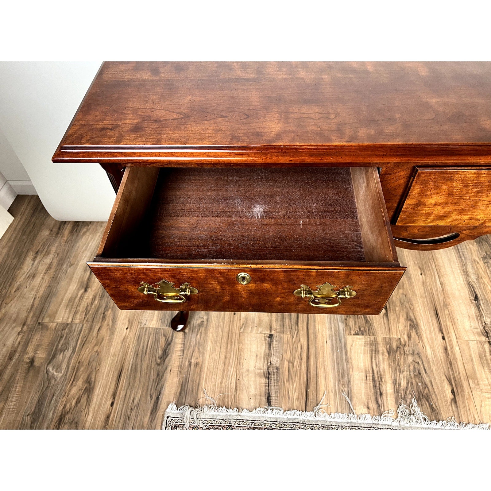 The Henredon Vintage Solid Cherry Queen Anne Style Sideboard, featuring an open top drawer, brass handles, and a shiny finish, is displayed on a wood floor beside a white rug.