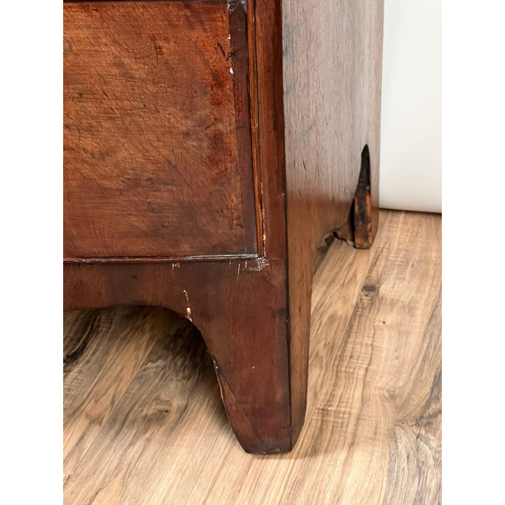 Close-up of the lower corner of an Antique George III Mahogany Bowfront Chest on French feet (late 18th century), showing scratches, wear, curved foot, vertical carved detail, and classic Georgian styling. Brand: Unknown.