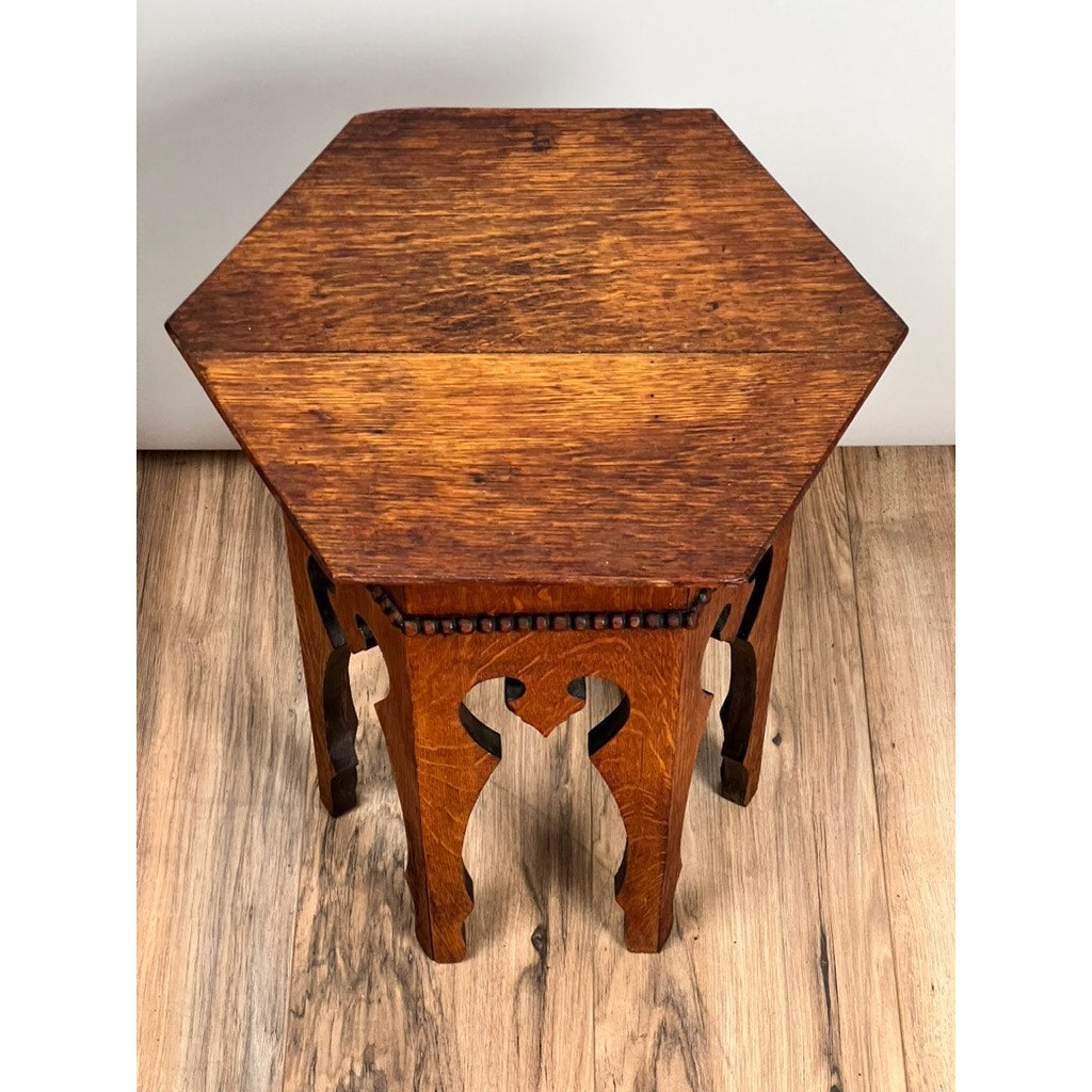 Antique Arts & Crafts Small Oak Occasional Table c. 1910 with hexagonal surface, ornate carved legs, and rich wood grain shows classic wear. Shown on a wood floor against a plain white background; brand unknown.