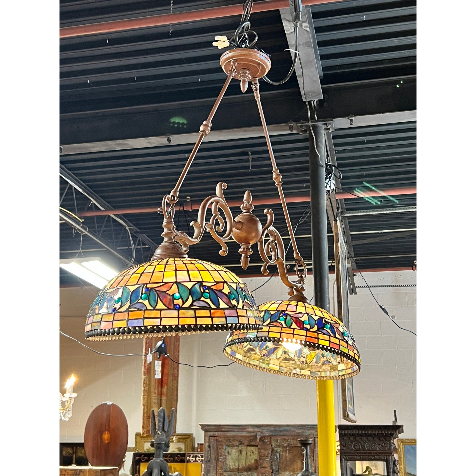 Two Vintage Tiffany Style Leaded Stained Glass Double Pendant Billiard Island Lights, featuring vibrant geometric and floral patterns, hang from bronze fixtures to create a stunning vintage pendant light display above a kitchen island in an industrial-inspired indoor space.