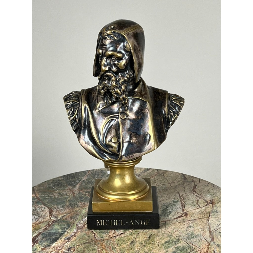 A patinated bronze sculpture of Michelangelo by Albert-Ernest Carrier-Belleuse, modeled before 1883 in Paris, stands on a gold and black pedestal atop a round marble table against a white background.