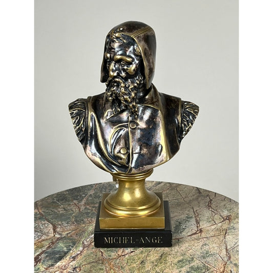 Patinated bronze sculpture of Michelangelo by Albert-Ernest Carrier-Belleuse, modeled before 1883 in Paris and offered by Pearl City Antiques, featuring a bronze-colored bust of a bearded man with a hood labeled “MICHEL-ANGE,” displayed on a round, marble-patterned surface against a plain background.
