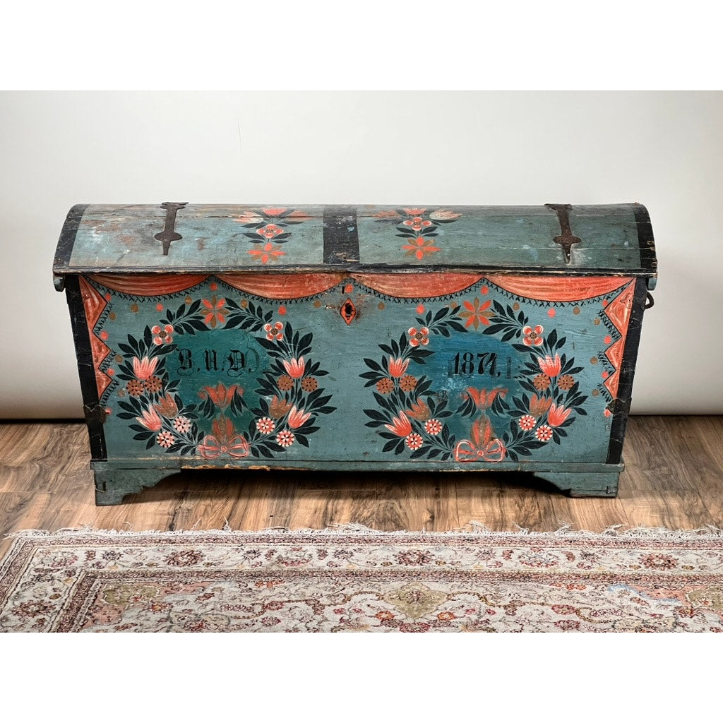 An Antique Swedish Oak Kista Dowry Chest c. 1841, in teal with black, red, and orange floral designs, exemplifies Swedish folk art and sits on a wooden floor beside a patterned rug. Brand: None/Unknown.